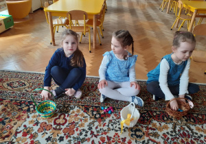 Dzieci siedzą na dywanie. Układają i liczą czekoladowe jajeczka otrzymane od WIelkanocnego Zajączka