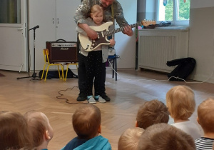 Dziewczynka gra na gitarze z pomocą muzyka