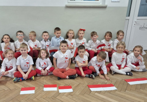 Zdjęcie grupowe dzieci z grupy III w biało - czerwonych strojach. Dzieci siedzą w dwóch rzędach i czekają na rozpoczęcie uroczytości