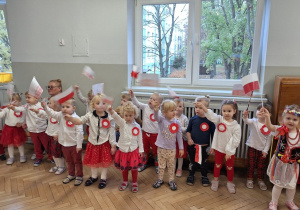 Dzieci śpiewają piosenkę i tzrymają w dłoni flagi wysoko uniesione w górę