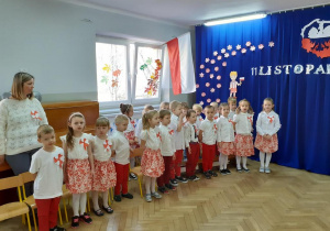 Dzieci ubrane na biało czerwono śpiewają piosenkę na tle dekoracji święta 11 listopada