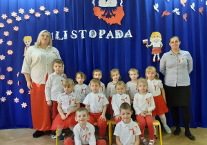 Dzieci z grupy Biedronki wraz z nauczycielkami pozują do zdjęć na tle dekoracji na 11 listopada