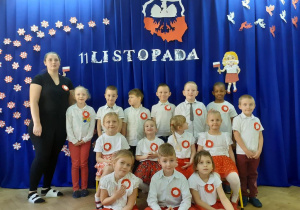 Dzieci z grupy Motylki wraz z nauczycielką pozują do zdjęć na tle dekoracji na 11 listopada
