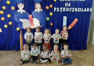 Dzieci pozują do zdjęcia na tle dekoracji z dyplomami w rękach