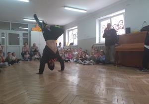 Dzieci spiedzą i oglądają pokaz tańca breakdance