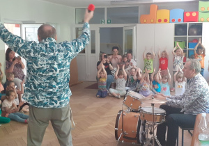 Muzyk gra na perkusji, dzieci klaszczą do rytmu.