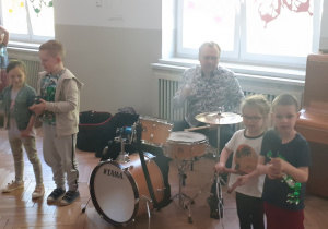 Dzieci stoja i graja na instrumentach perkusyjnych, Pan gra na perkusji.