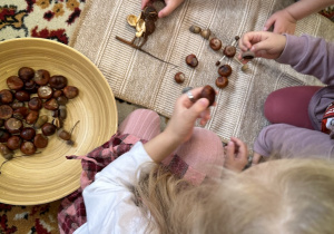 Dzieci układają obrazy na dywaniku z jesiennych skarbów - kasztanów, żołędzi i liści