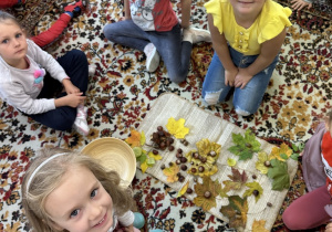 Dzieci układają obrazy na dywaniku z jesiennych skarbów - kasztanów, żołędzi i liści