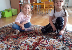 Dziewczynki siedzą na dywanie i przeliczają zebrane kasztany