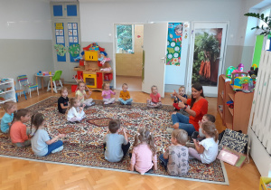 Dzieci siedzą na dywanie i uczestniczą w zabawie na zajęciach języka angielskiego