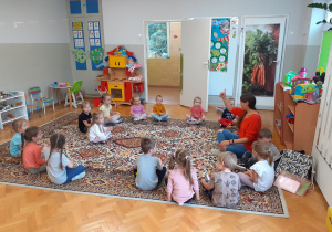 Dzieci siedzą na dywanie i uczestniczą w zabawie na zajęciach języka angielskiego