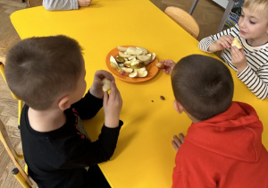 Dzieci siedzą przy stolikach i próbują owoce i warzywa