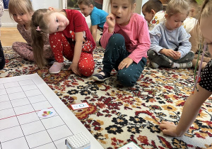 Dzieci siedzą na dywanie i po kolei programują robota za pomocą kart