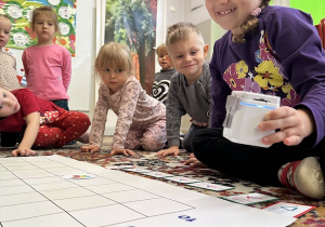 Dzieci siedzą na dywanie i po kolei programują robota za pomocą kart,tak by zebrał wszystkie baloniki