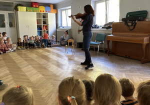 dzieci siedzą na sali i słuchają utworu granego na skrzypcach