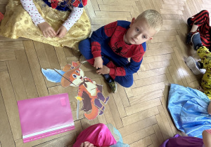 dzieci siedzą na podłodze i składają obrazki pocięte na części