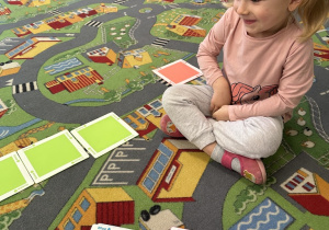 Dziewczyna siedzi na dywanie i układa kolorowe kartoniki