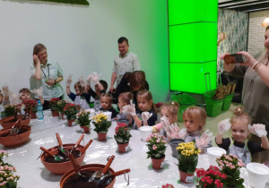 dzieci siedzą przy stole i zakładają rękawiczki aby przesadzać kwiatki