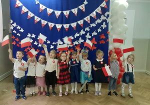 Dzieci pozują do zdjęcia na tle dekoracji w biało czerwonych barwach , trzymają w rękach flagi polski