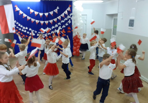Dzieci wykonują układ taneczny z biało czerwonymi flagami w rękach