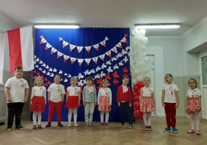 Dzieci recytują wiersz do na tle dekoracji w biało czerwonych barwach