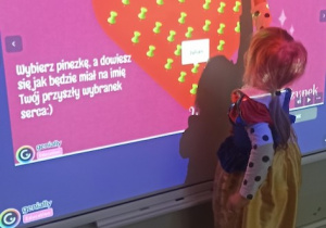 Dziewczynka wykonuje andrzejkowa wróżbę na tablicy multimedialnej