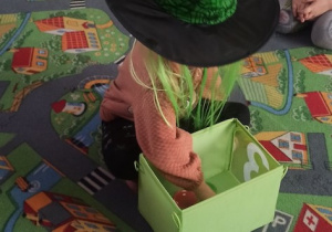 Dziecko siedzi na dywanie i z kapeluszem. Czarownicy wybiera los z zielonego pudelka w zabawie .
