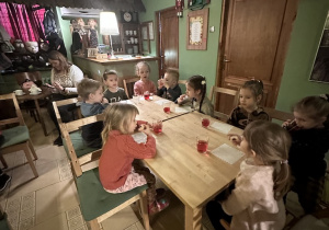 dzieci siedzą przy stolikach jedzą ciasteczka i piją soczek