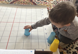 dziecko układa wieżę z kolorowych kubeczków na macie do kodowanie