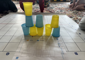 dziecko układa wieżę z kolorowych kubeczków na macie do kodowanie