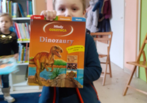 Antoś pokazuje książkę o dinozaurach, którą sobie wybrał.