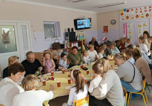 Dzieci siedzą przy stole z Babciami i Dziadkami podczas poczęstunku.