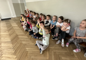 dzieci siedzą na sali gimnastycznej i słuchają koncertu
