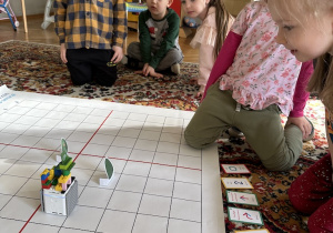 dzieci siedzą na dywanie i programują robota edukacyjnego według określonych kryteriów