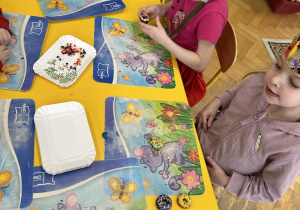dzieci siedzą przy stolikach i lepią paczki z plasteliny