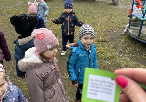 dzieci wykonują zadania z gry terenowej - szukają karteczek z zadaniami w ogrodzie