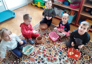 Dzieci siedzą na dywanie. Układają i liczą czekoladowe jajeczka otrzymane od WIelkanocnego Zajączka