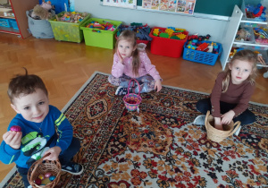 Dzieci siedzą na dywanie. Układają i liczą czekoladowe jajeczka otrzymane od WIelkanocnego Zajączka