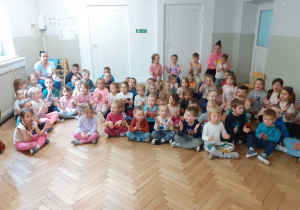 Dzieci siedzą i śpiewają razem z prowadzącym piosenkę powitalną