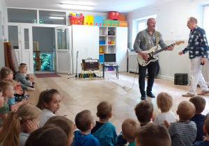 Muzyk z prowadzącym opowiadają dzieciom o gitarze elaktrycznej