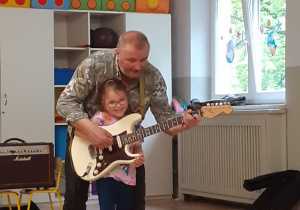 Dziewczynka gra na gitarze z pomocą muzyka