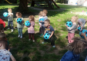 Dzieci stoją w kole i próbują podrzucać i łapać piłkę