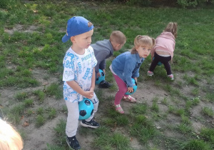 Dzieci próbują poruszać się trzymając piłkę między kolanami