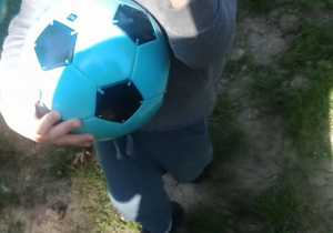 Chłopiec stoi i trzyma piłkę, pokazuję znalezione piórko