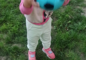 Dziewczynka stoi na trawie i podrzuca piłkę