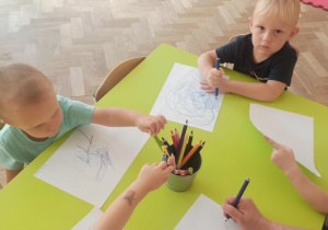 Dzieci siedzą przy stoliczku i rysują kredkami ołówkowymi