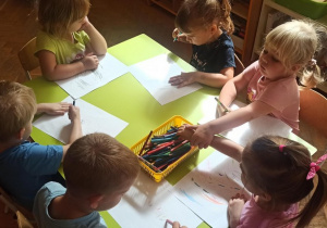Dzieci siedzą przy stoliczku i rysują kredkami ołówkowymi