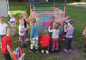 Na zdjęciu widać grupę dzieci jak malują kolorowy świat za pomoca swoich dłoni, kolorowymi farbami na foli rozciągniętej na drabinkach