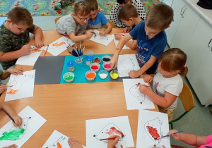 Dzieci siedzą przy stole i maluja farbami zwierzątka